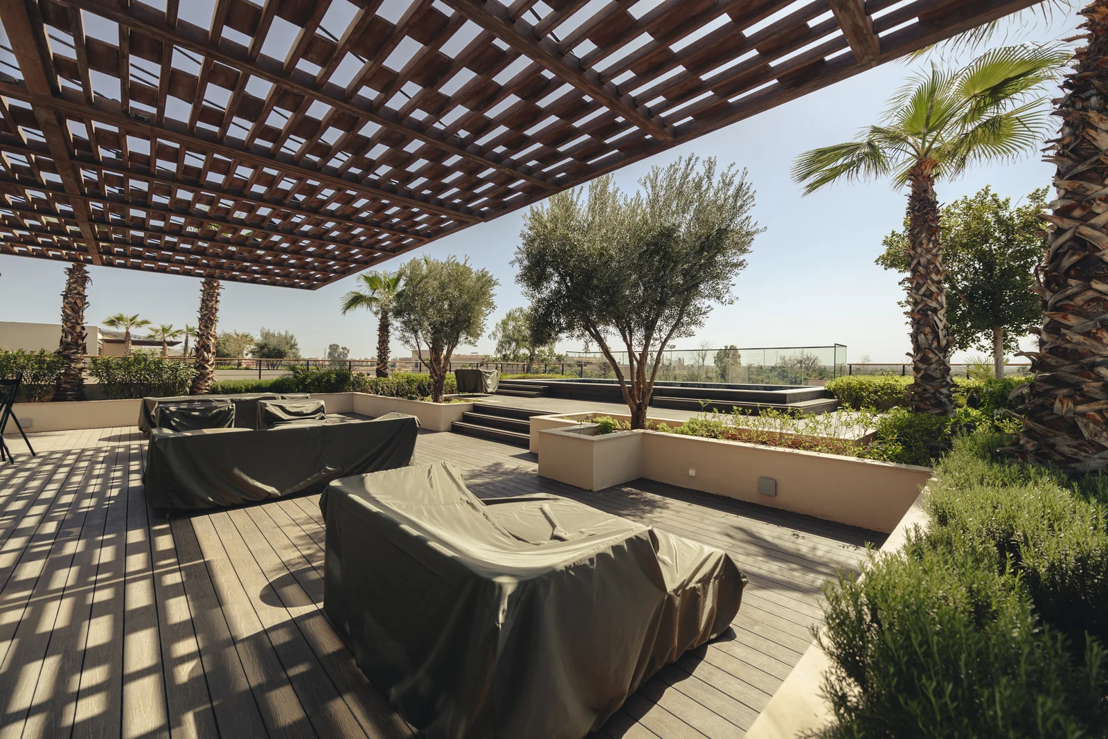 Covered daybeds on a rooftop terrace under a wooden pergola, a home kept ready while its owners live abroad part of the year
